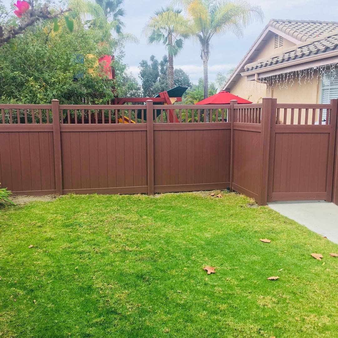 A brown wooden fence surrounds a lush green yard in front of a house.