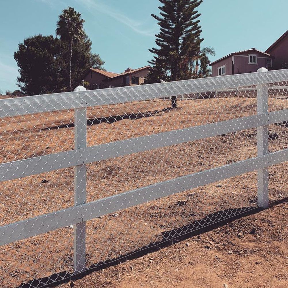 A white fence surrounds a dirt field with houses in the background