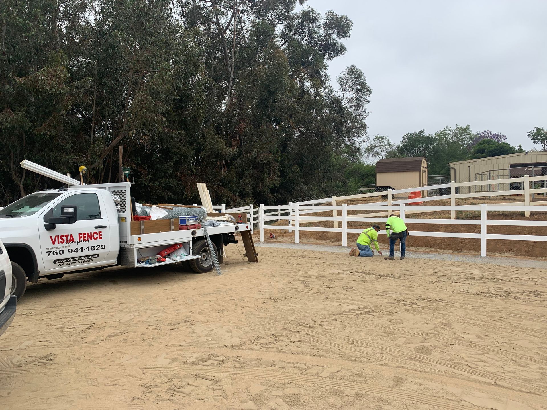A white truck is parked in a dirt field next to a white fence.