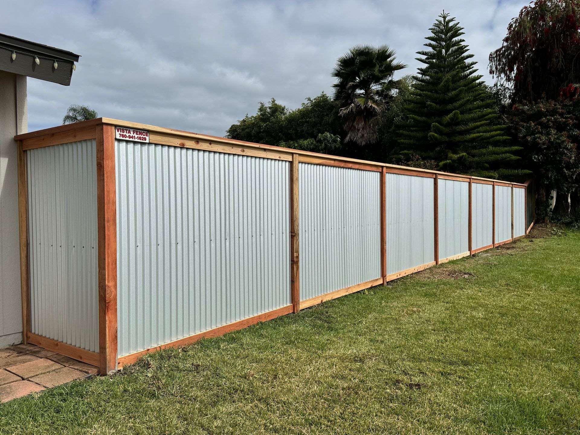A long white fence with wooden posts is sitting in the middle of a lush green field.