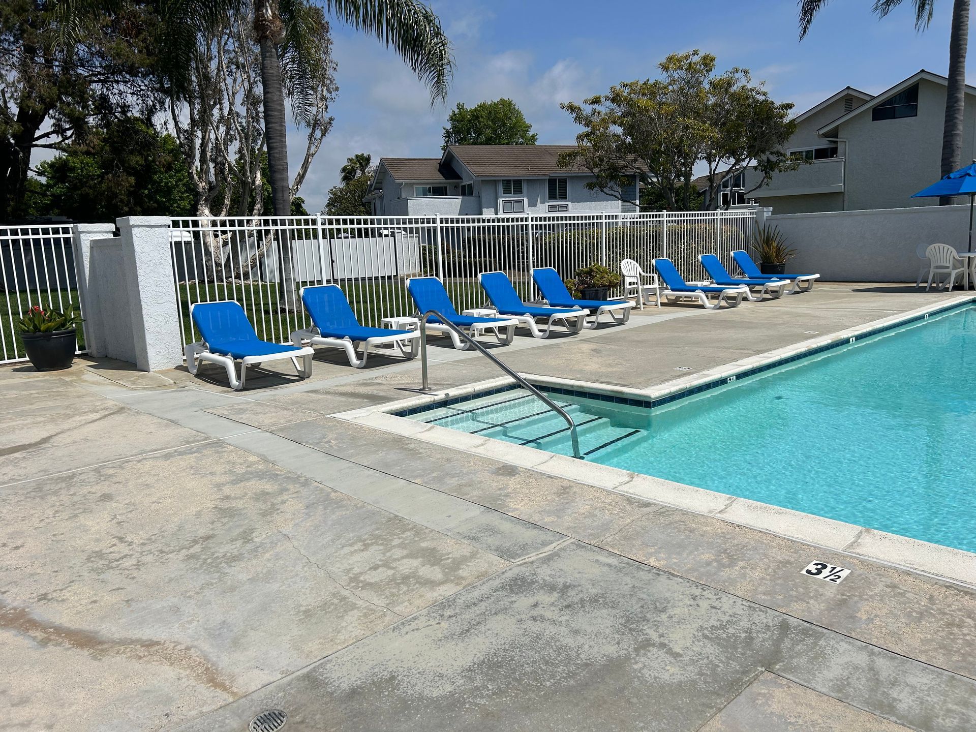 A swimming pool with blue chairs and umbrellas around it.