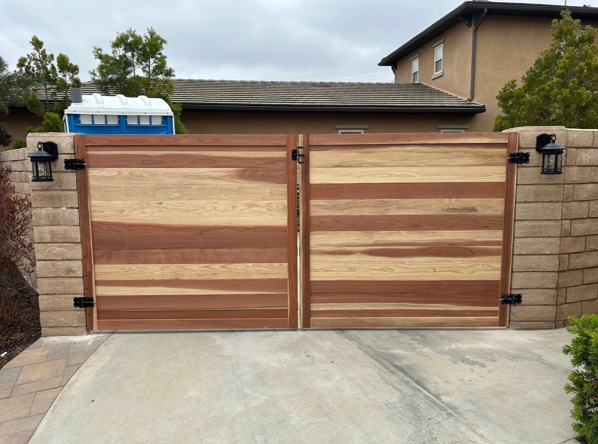 A wooden gate is open to a driveway in front of a house.