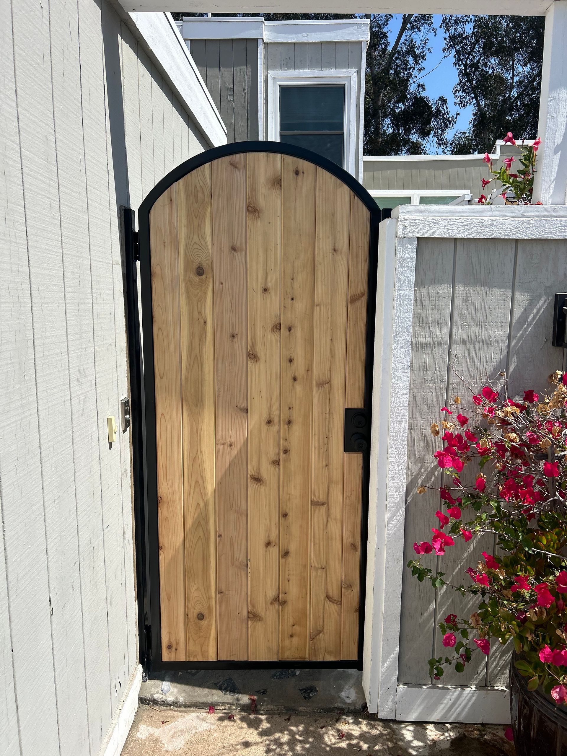 A wooden gate with a black frame is surrounded by flowers.