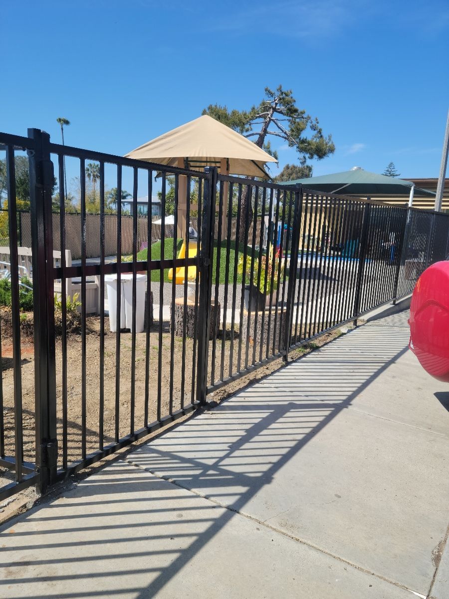 A red ball sits on the sidewalk next to a fence.