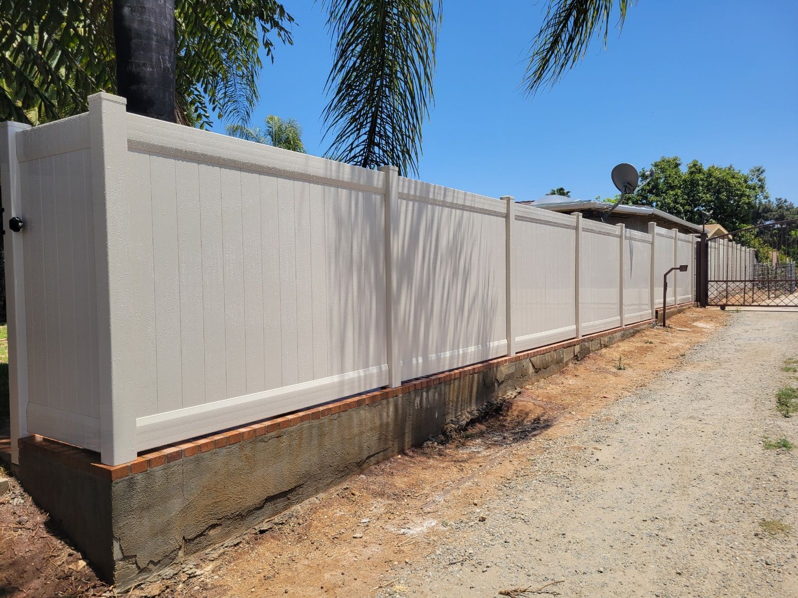 A white fence is along the side of a dirt road.