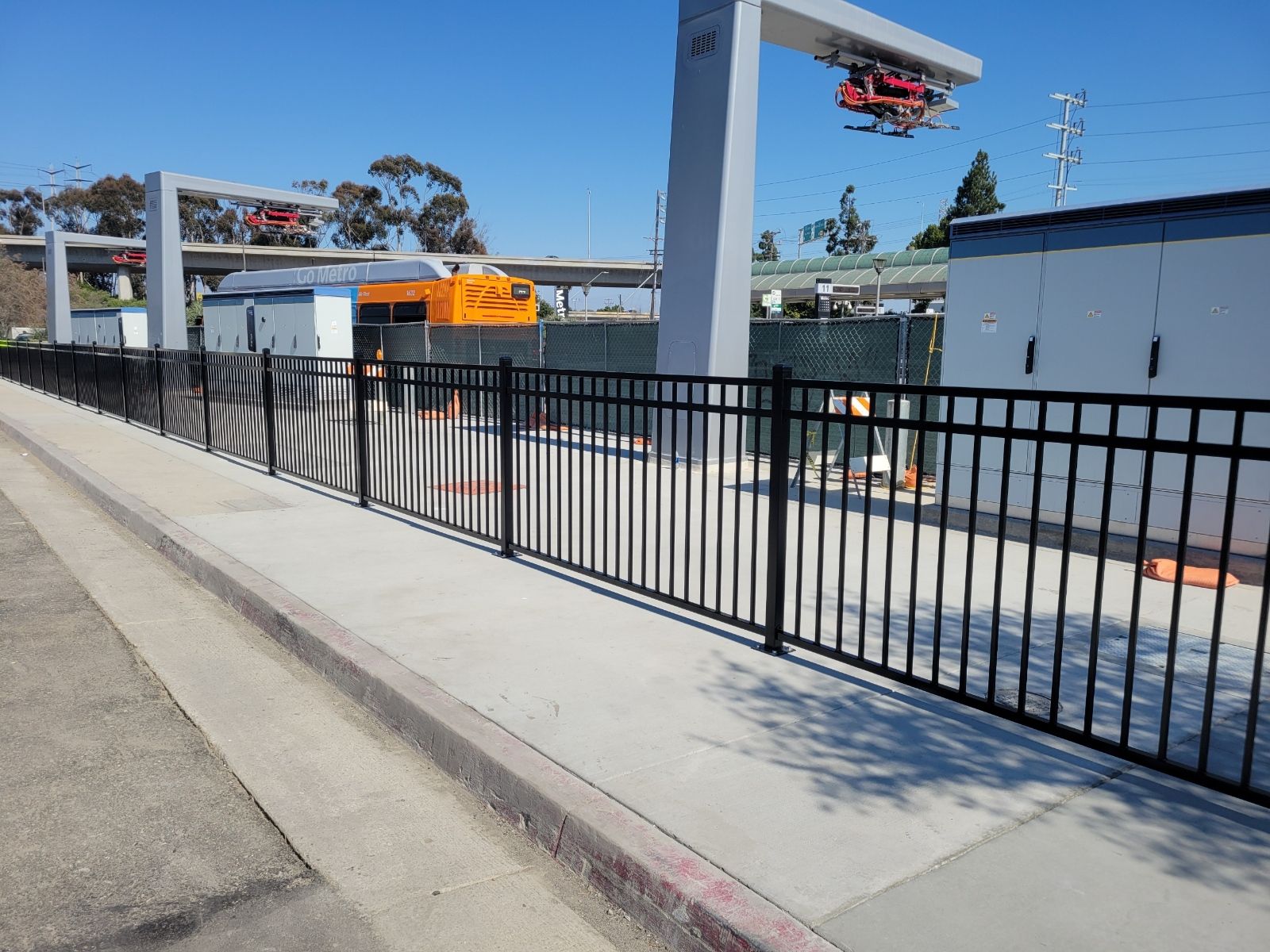 A black fence along a sidewalk with a bridge in the background.