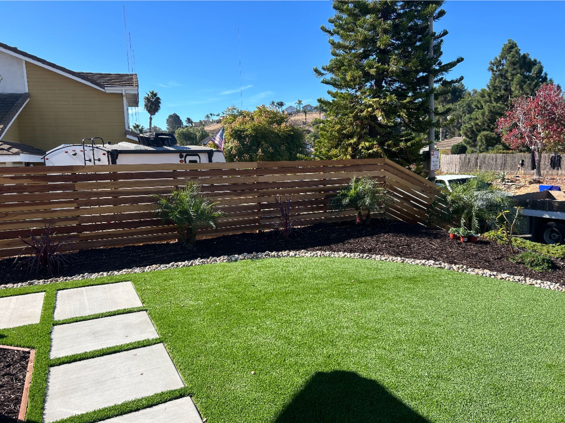 Backyard with green lawn, stone stepping path, and wooden fence under a clear blue sky