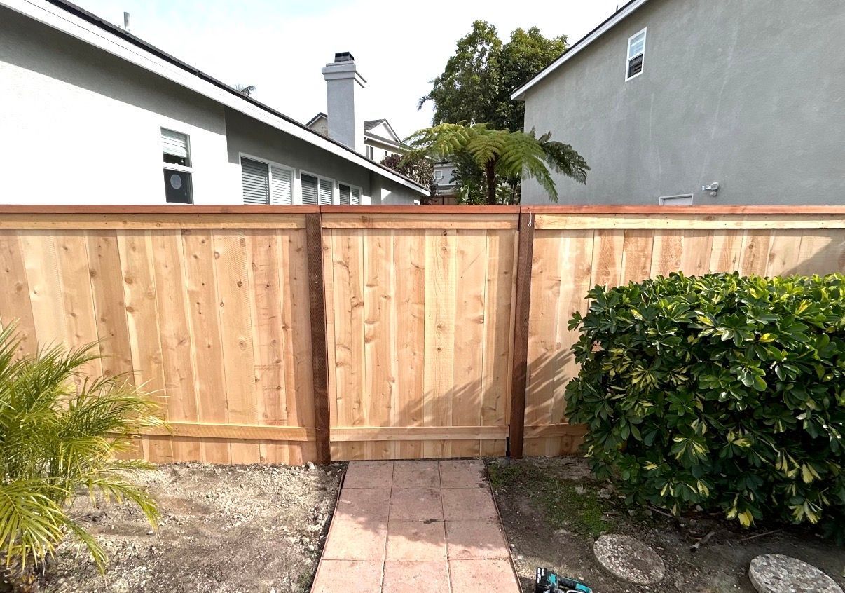 Wooden backyard gate and fence with stone path, shrubs, and neighboring house in the background