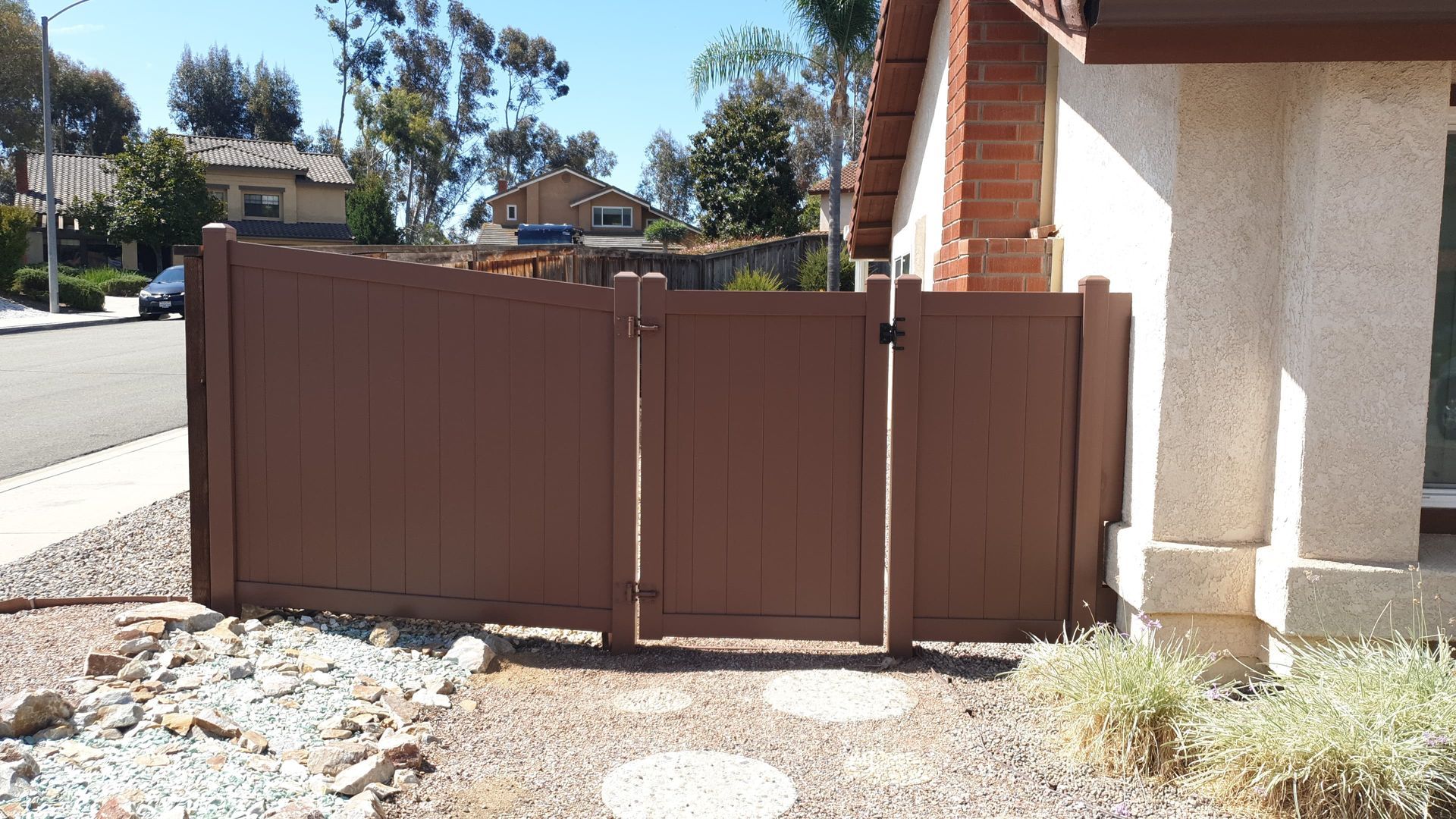 Brown fence and gate beside a stucco house on a sunny residential street.