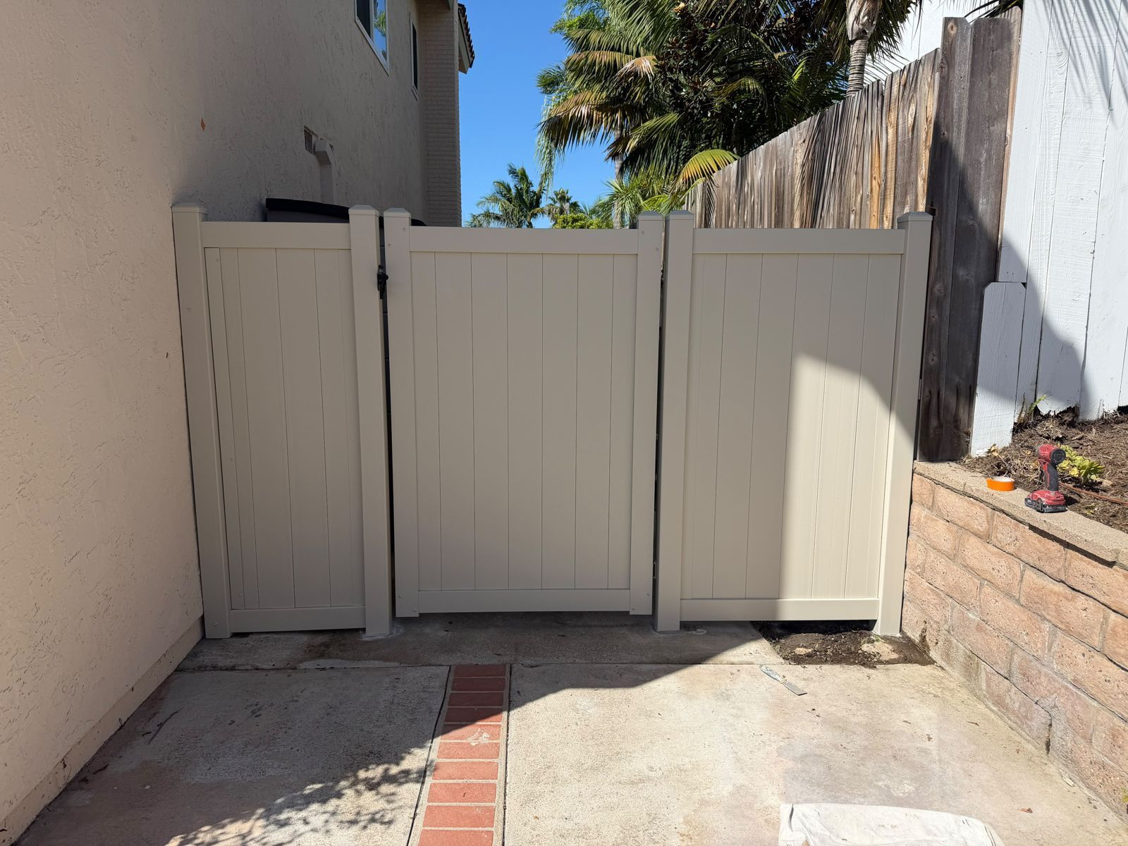 Beige wooden gate blocking a narrow outdoor walkway between stucco walls and a brick planter.