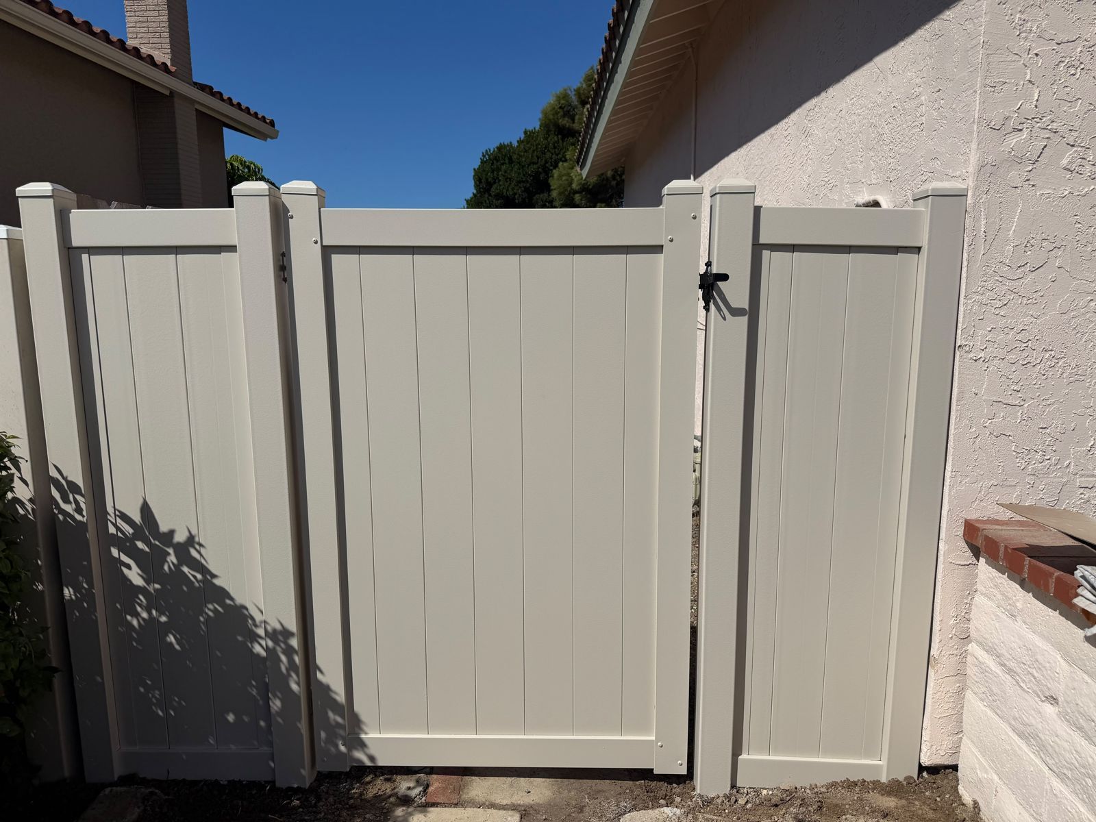 White wooden garden gate between stucco walls under a clear blue sky