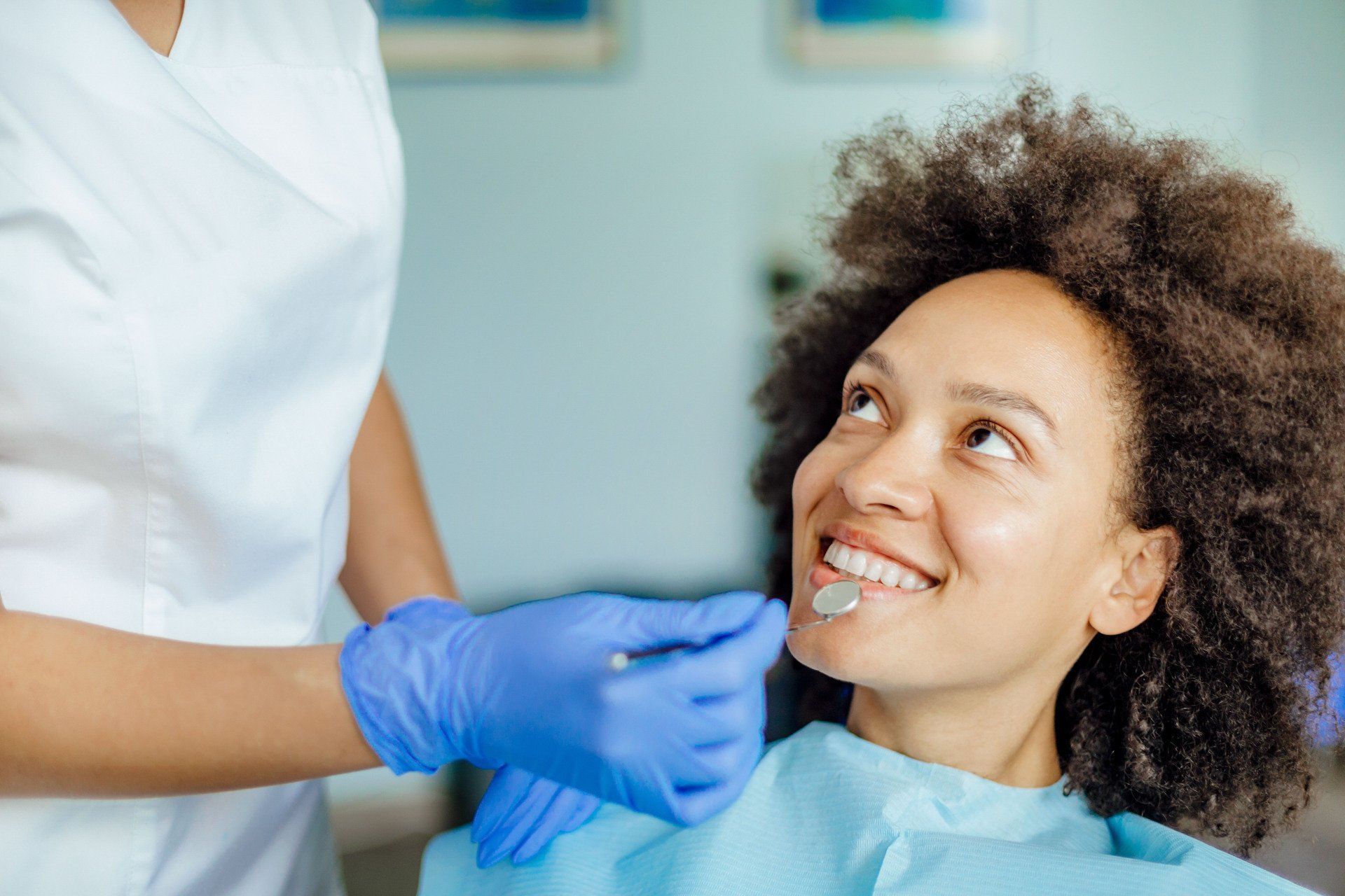 Dentist in blue gloves examining a smiling patient in a dental chair