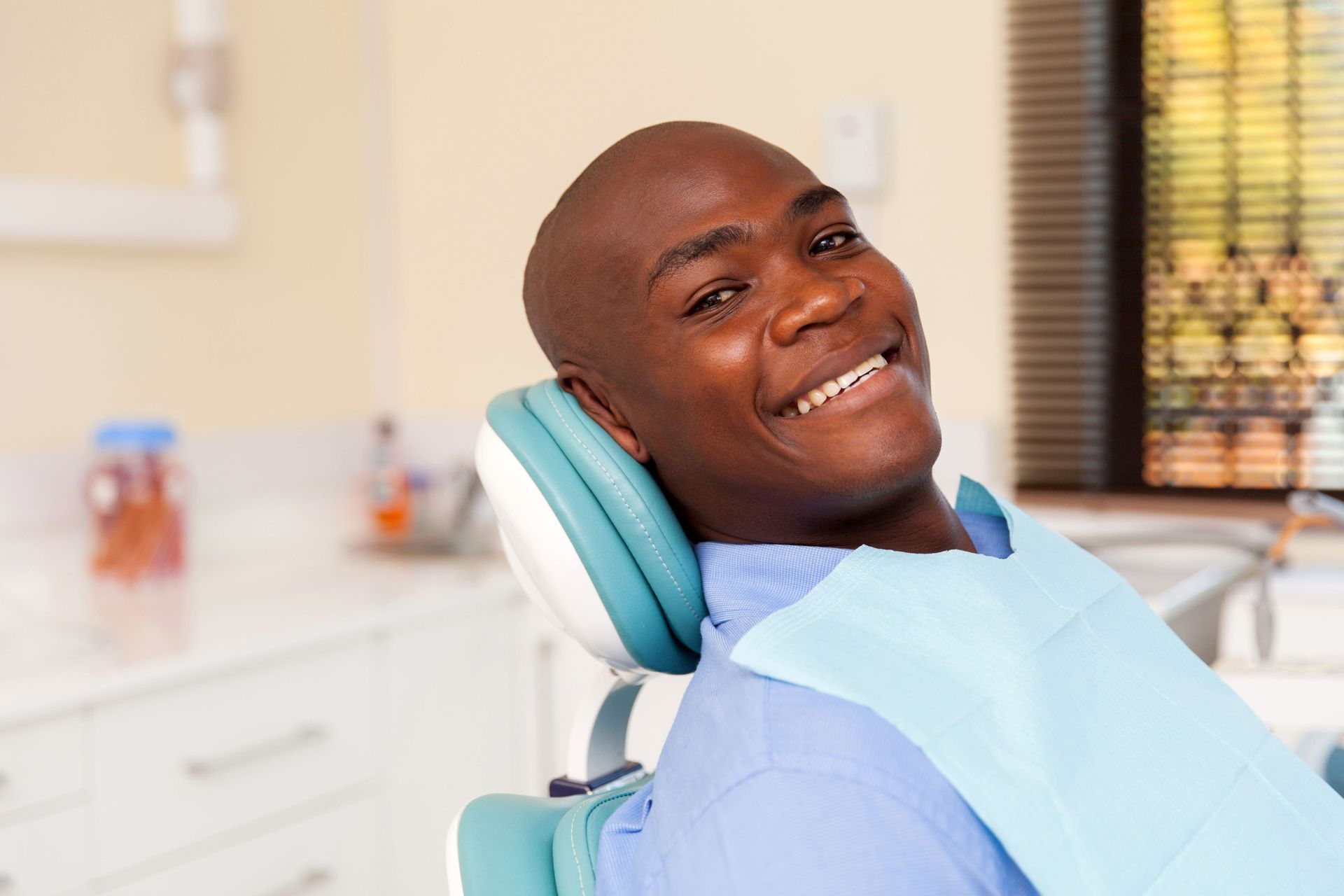 Smiling patient reclining in a dental chair with a blue bib in a bright clinic