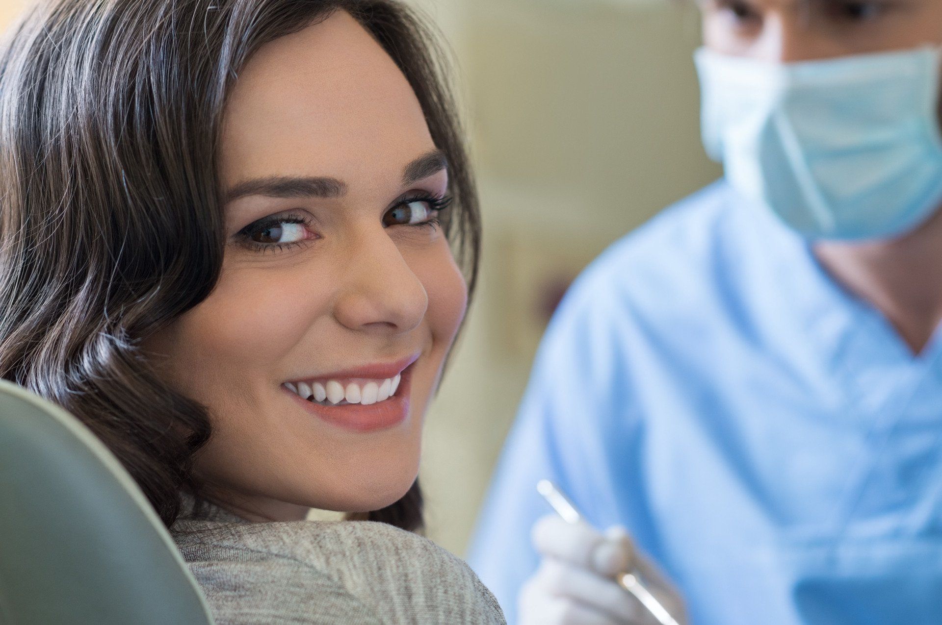 Smiling woman in a clinic with a masked healthcare worker in blue scrubs behind her
