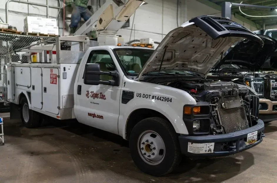 White utility truck with the hood up. In a garage, boom raised.