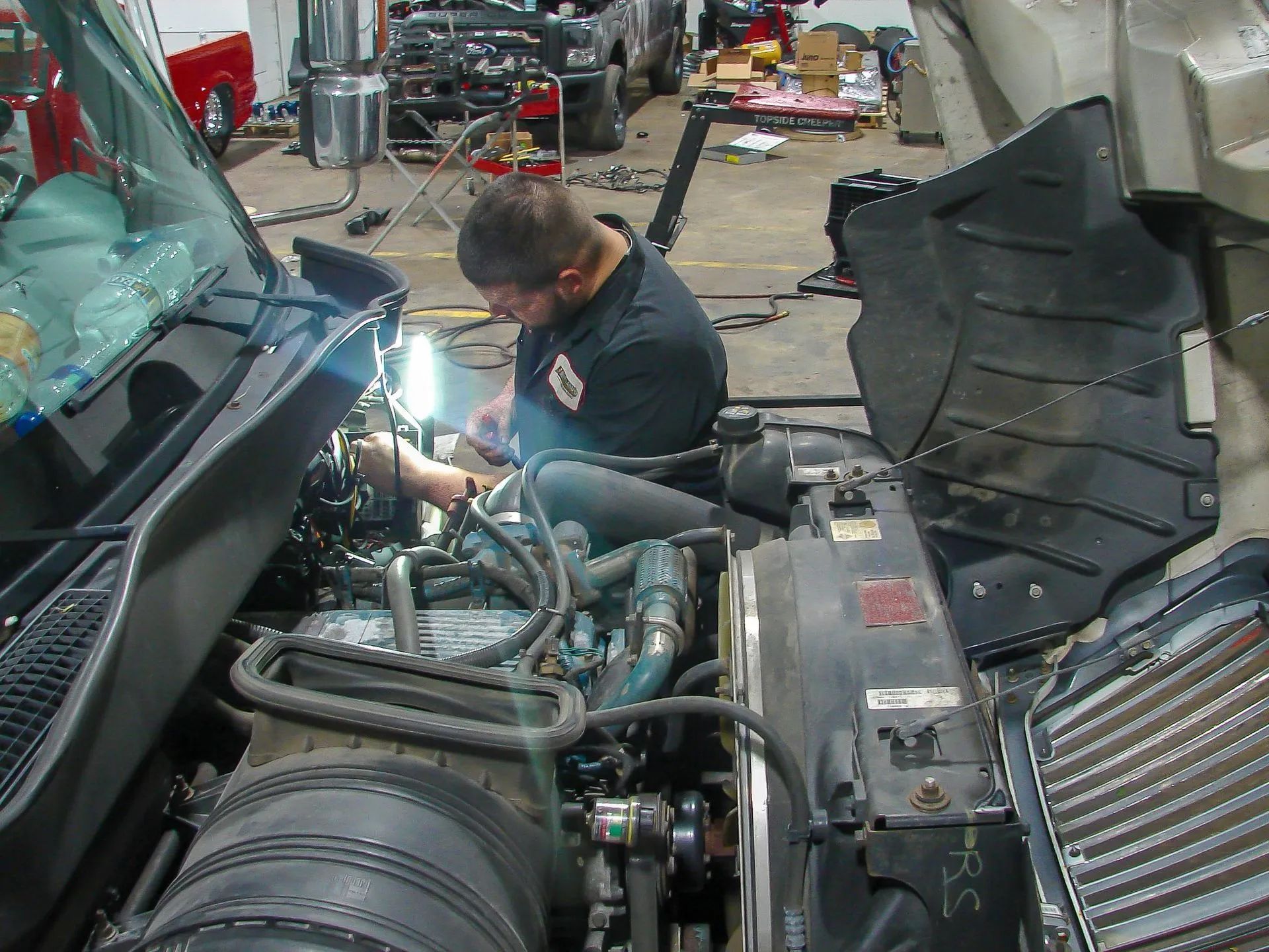 Mechanic working on a truck engine under the hood in a repair shop.