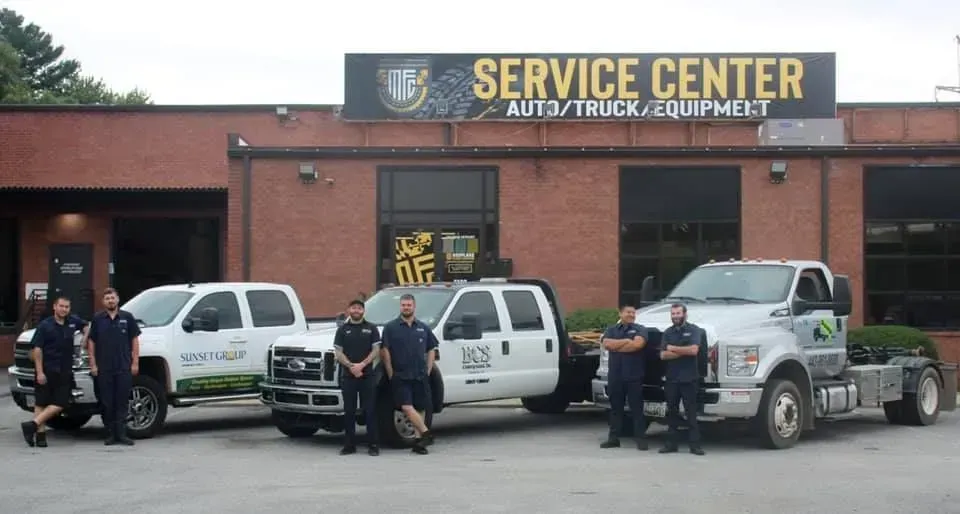 Team of mechanics in front of their auto/truck/equipment service center with trucks.