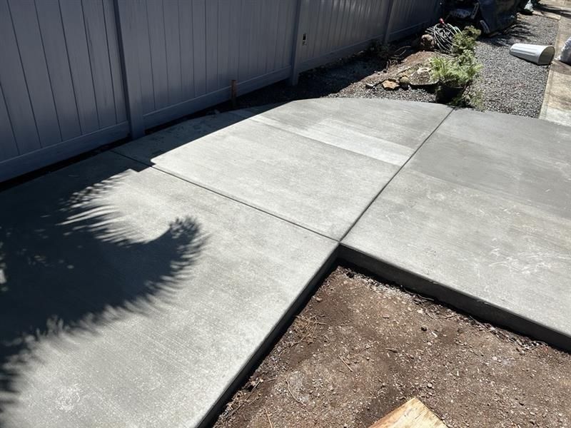 Backyard patio, a white house, and an orange hose on the concrete.
