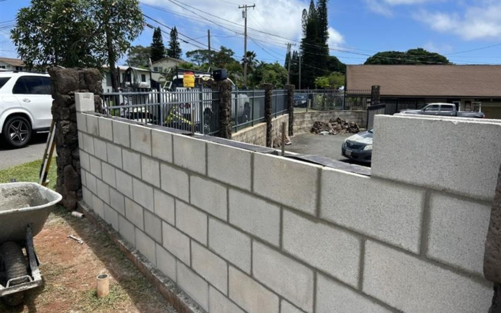 Partially built cinder block wall with metal fencing along a dirt roadside under a blue sky