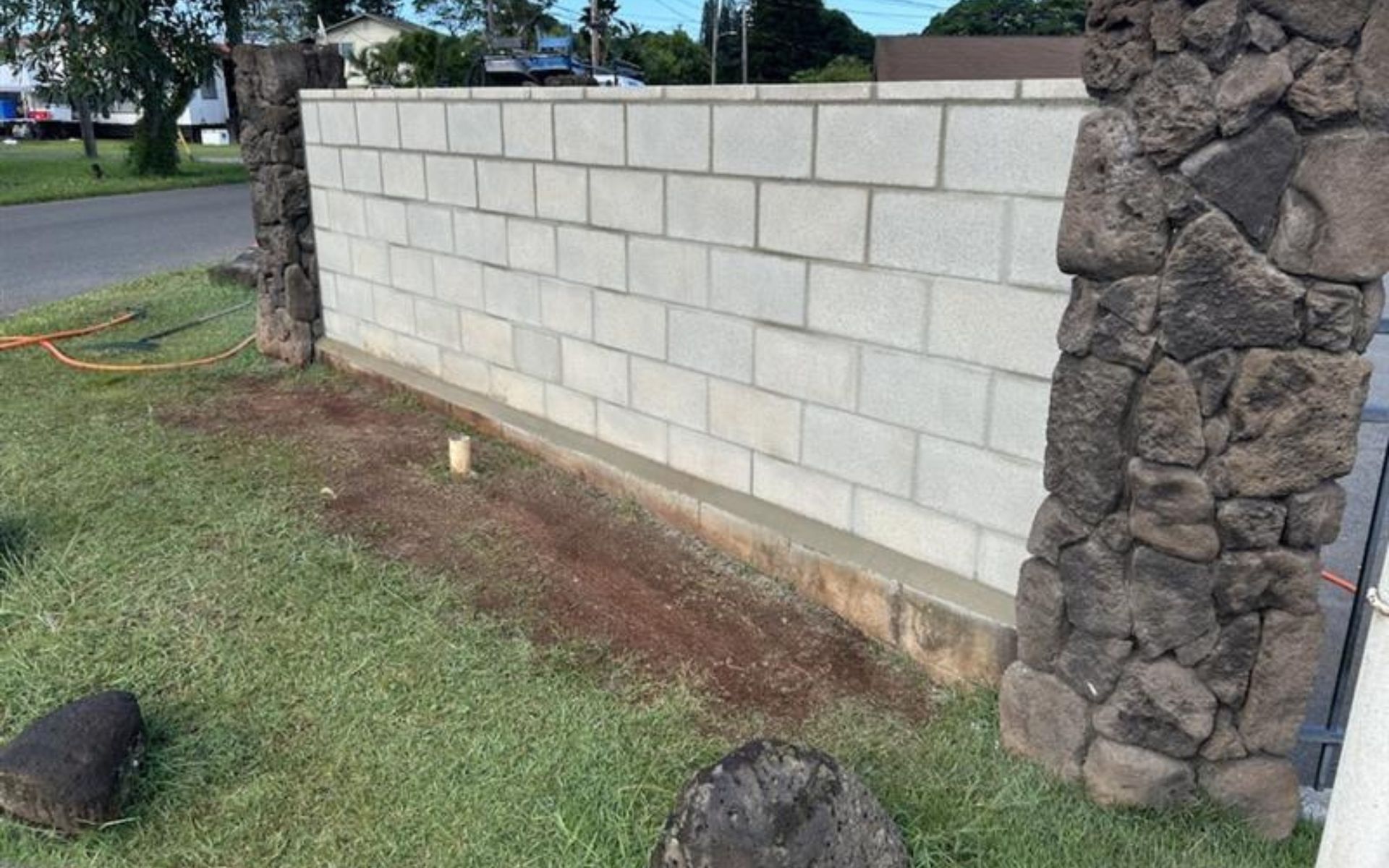 White block wall with stone pillar beside a grassy roadside slope