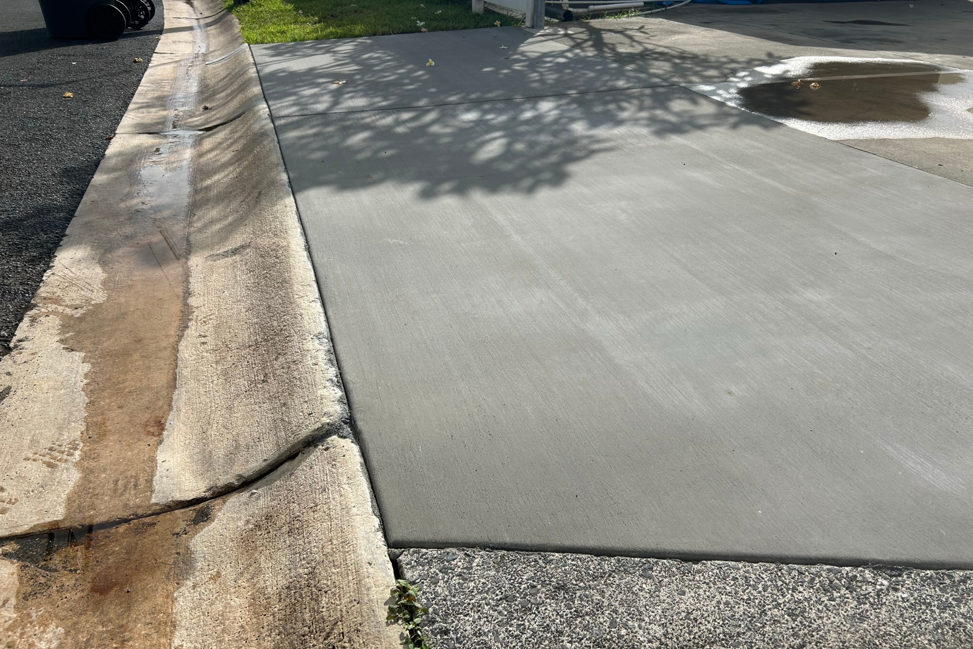 Sidewalk curb with a cracked edge beside a smooth concrete road in sunlight