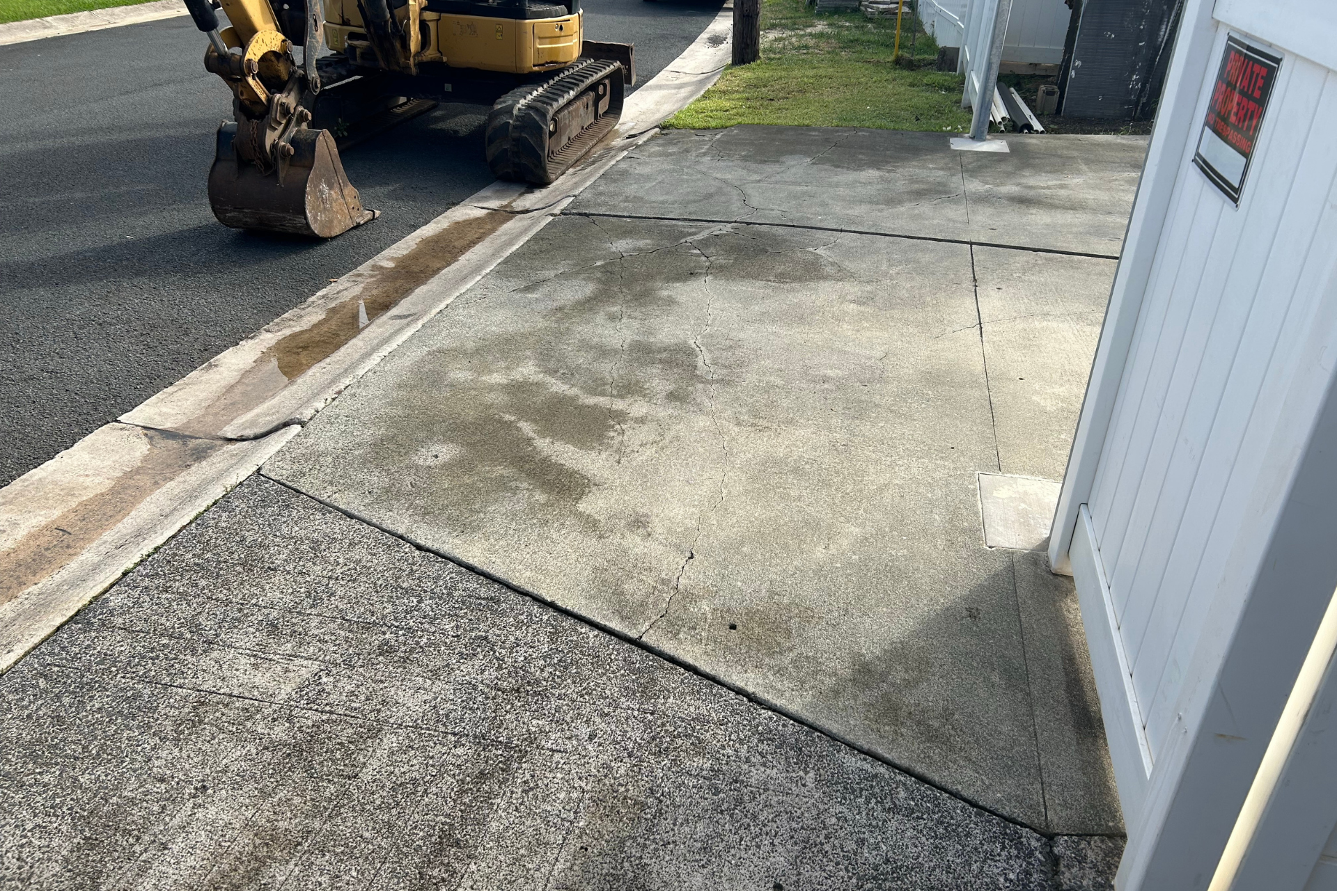 Construction equipment beside a cracked sidewalk and concrete driveway in front of a building