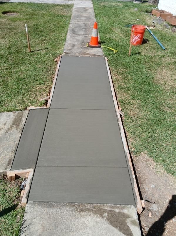 Freshly poured concrete sidewalk with orange cones and a caution bucket beside a grassy yard
