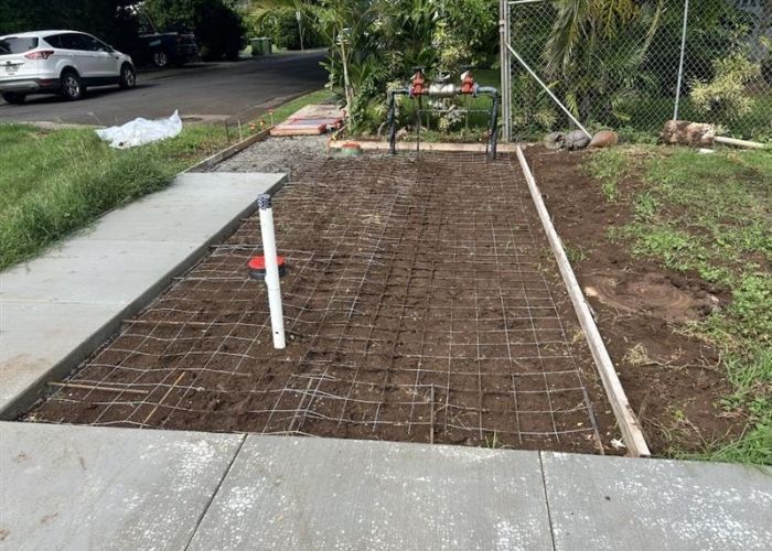 Freshly tilled garden bed beside a sidewalk, with a white stake and mesh fencing nearby