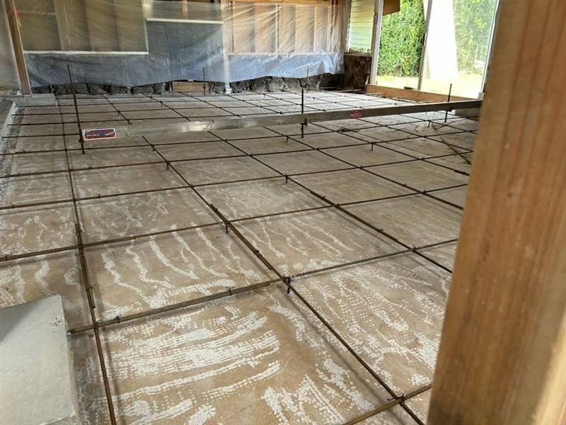 Large room under construction with a tiled floor covered in protective sheeting and a wooden support post
