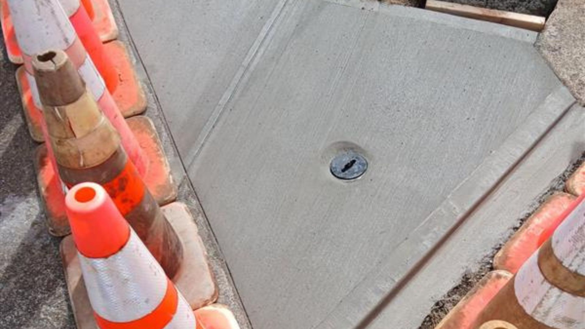 Fresh concrete slab with a central drain, bordered by orange traffic cones at the corners.