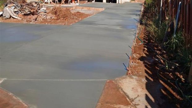 Fresh concrete driveway with expansion joints beside a dirt lot and fence under construction.