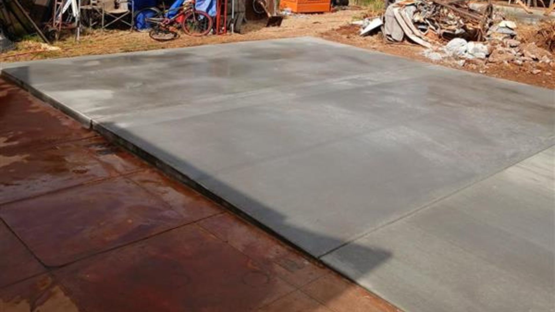 Freshly poured concrete slab beside a reddish-brown surface at a construction site