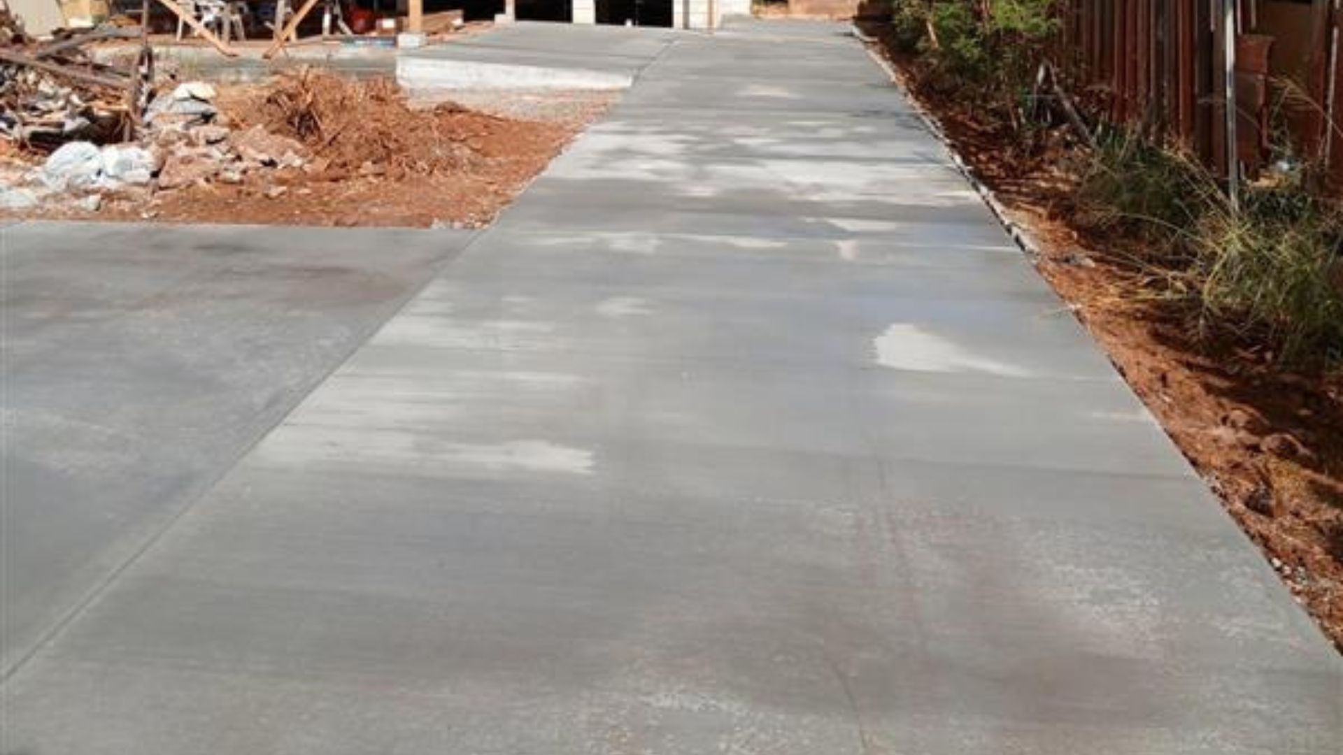 Freshly poured concrete driveway leading to a street, with dirt and construction debris on both sides
