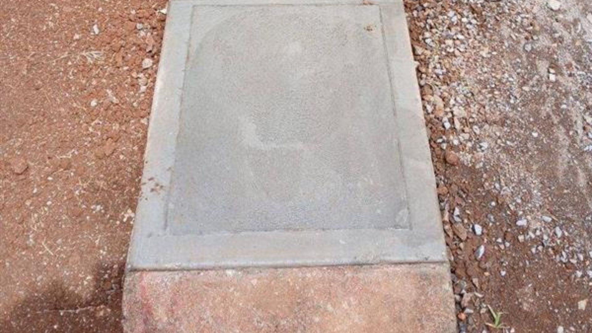 Concrete utility cover set in reddish gravel ground.