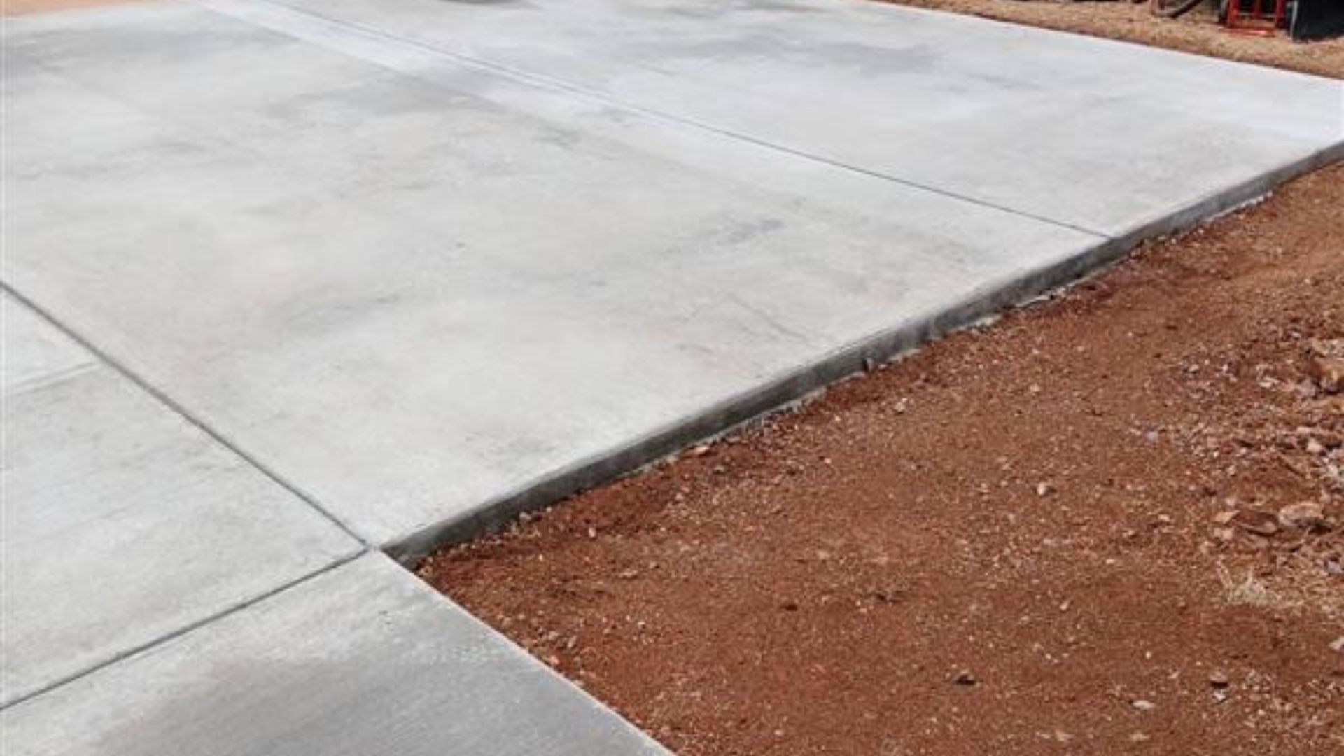 New concrete driveway slab beside red dirt soil patch