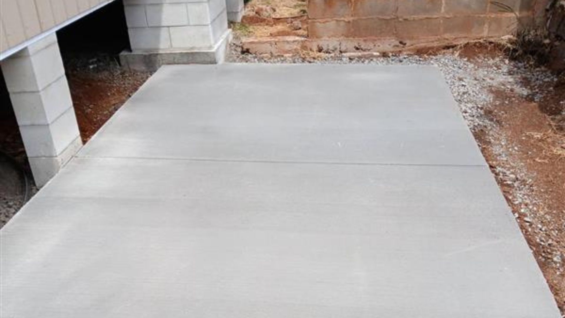 Newly poured concrete slab beside a building and dirt yard