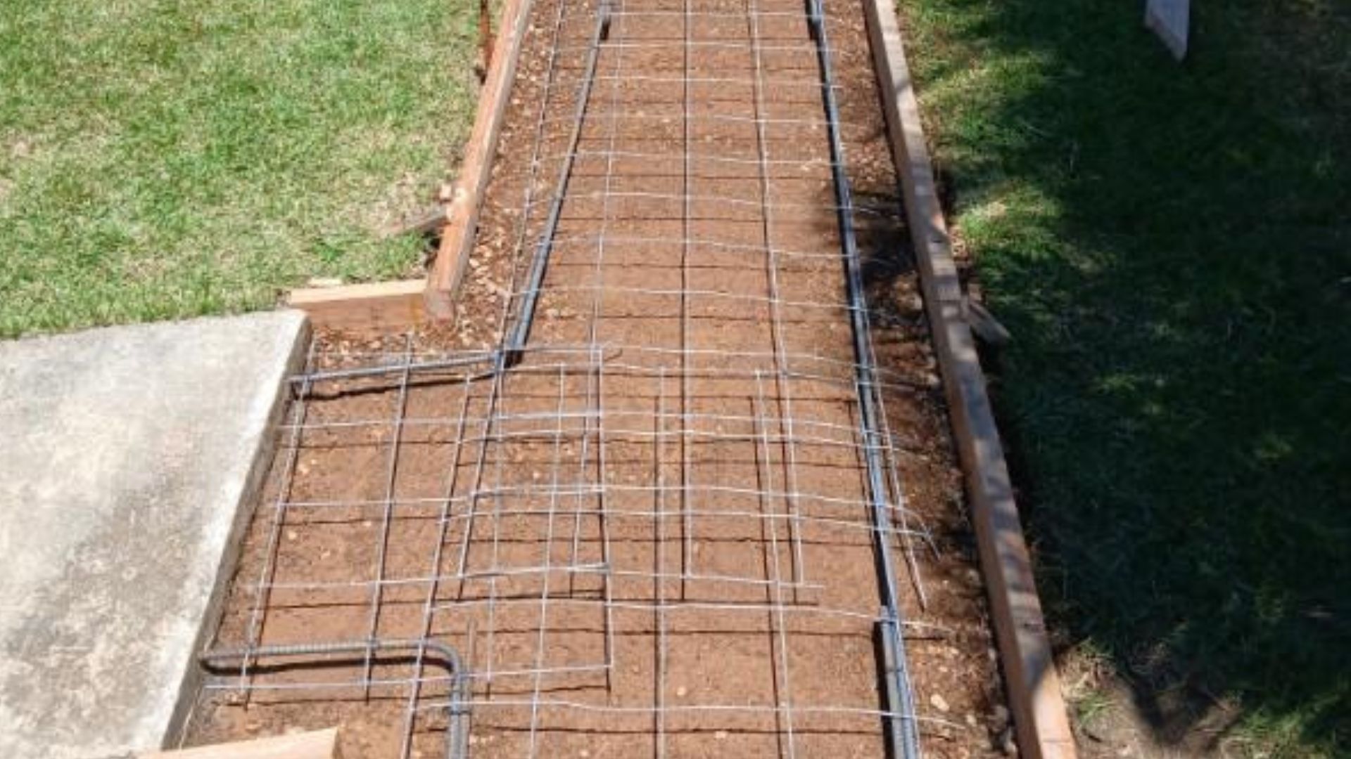 Concrete walkway under construction with steel rebar and wooden forms beside grass