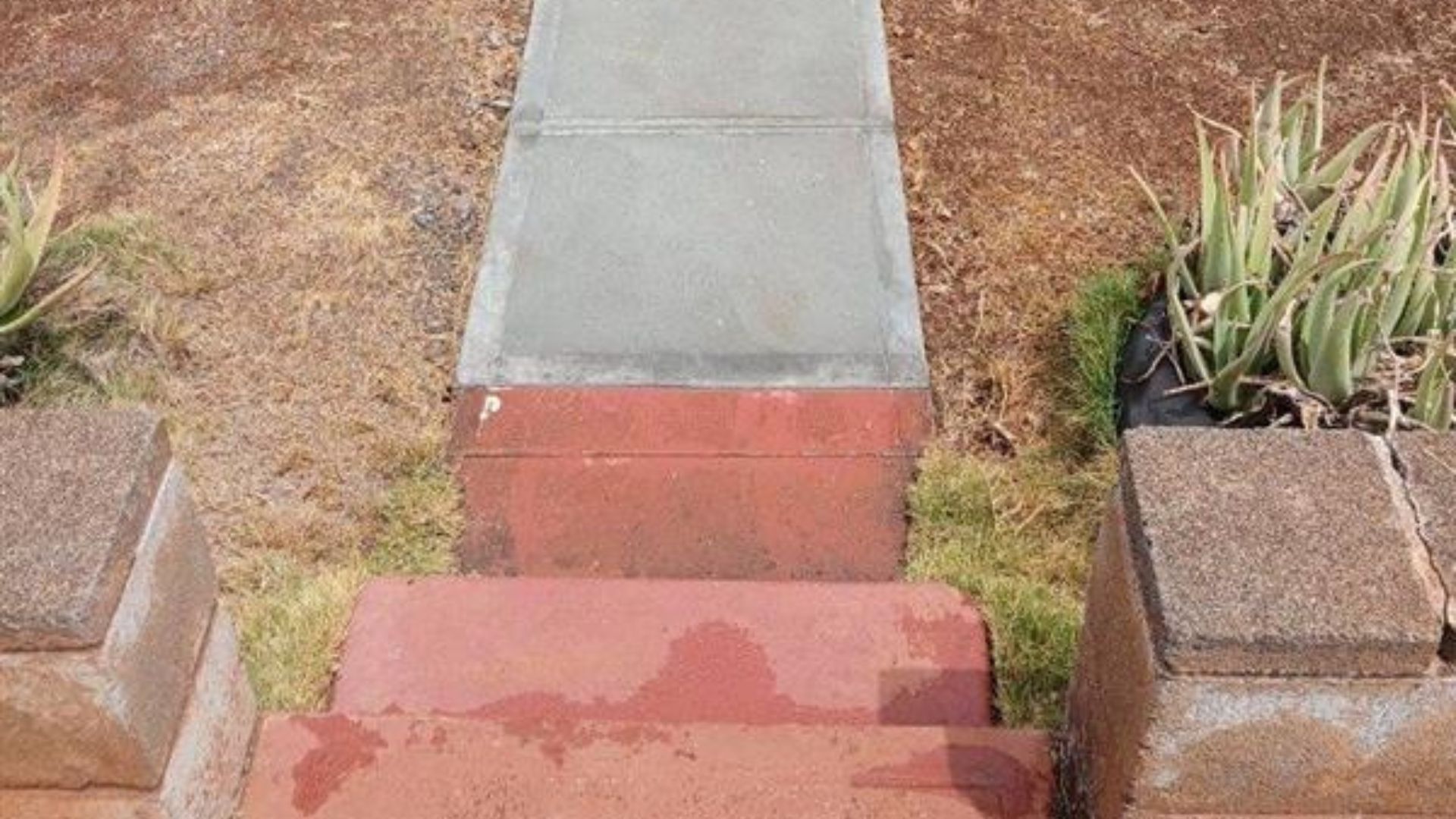 Concrete walkway with red steps leading through dry landscaping and planter boxes