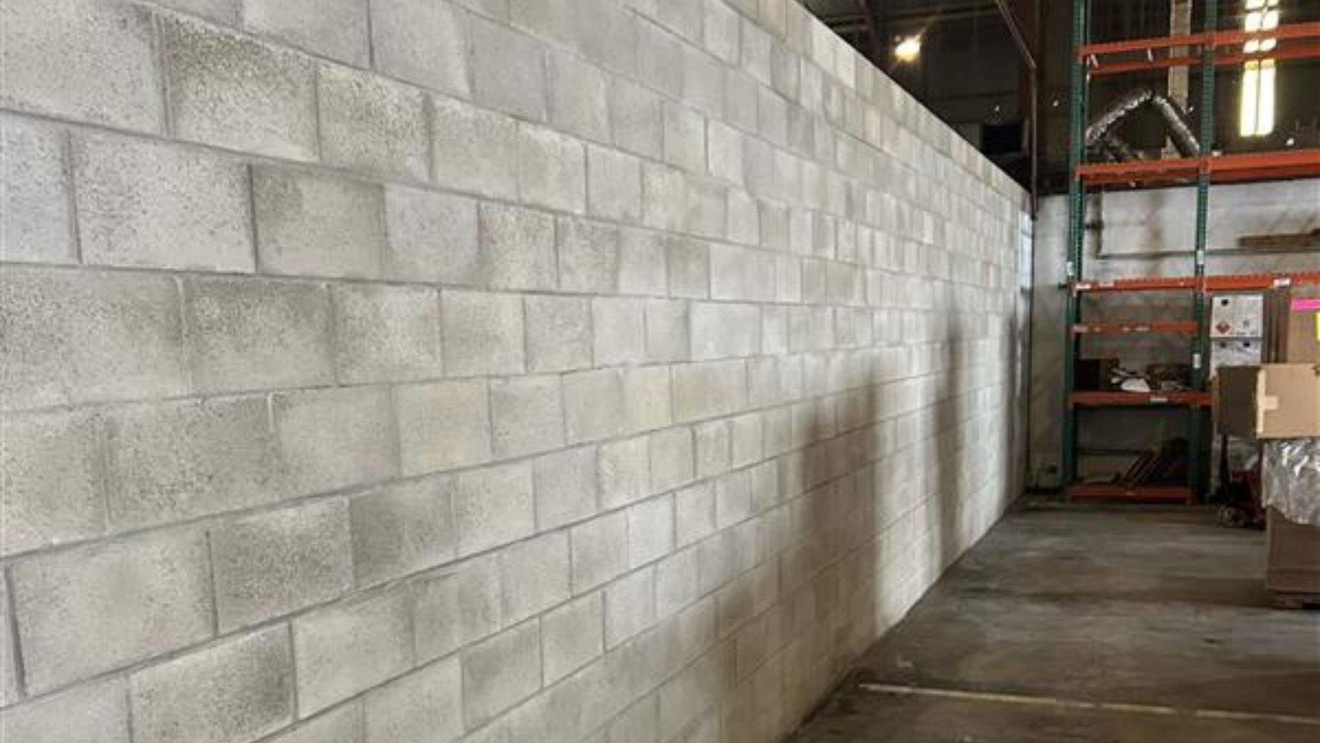 Long cinderblock wall inside an industrial warehouse aisle with stacked boxes and pallets