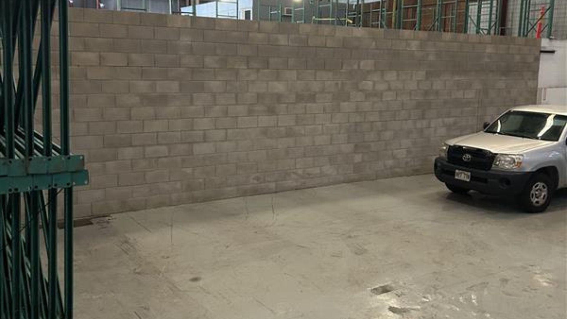 Parking area beside a tall concrete block wall, with a black SUV parked on the right.