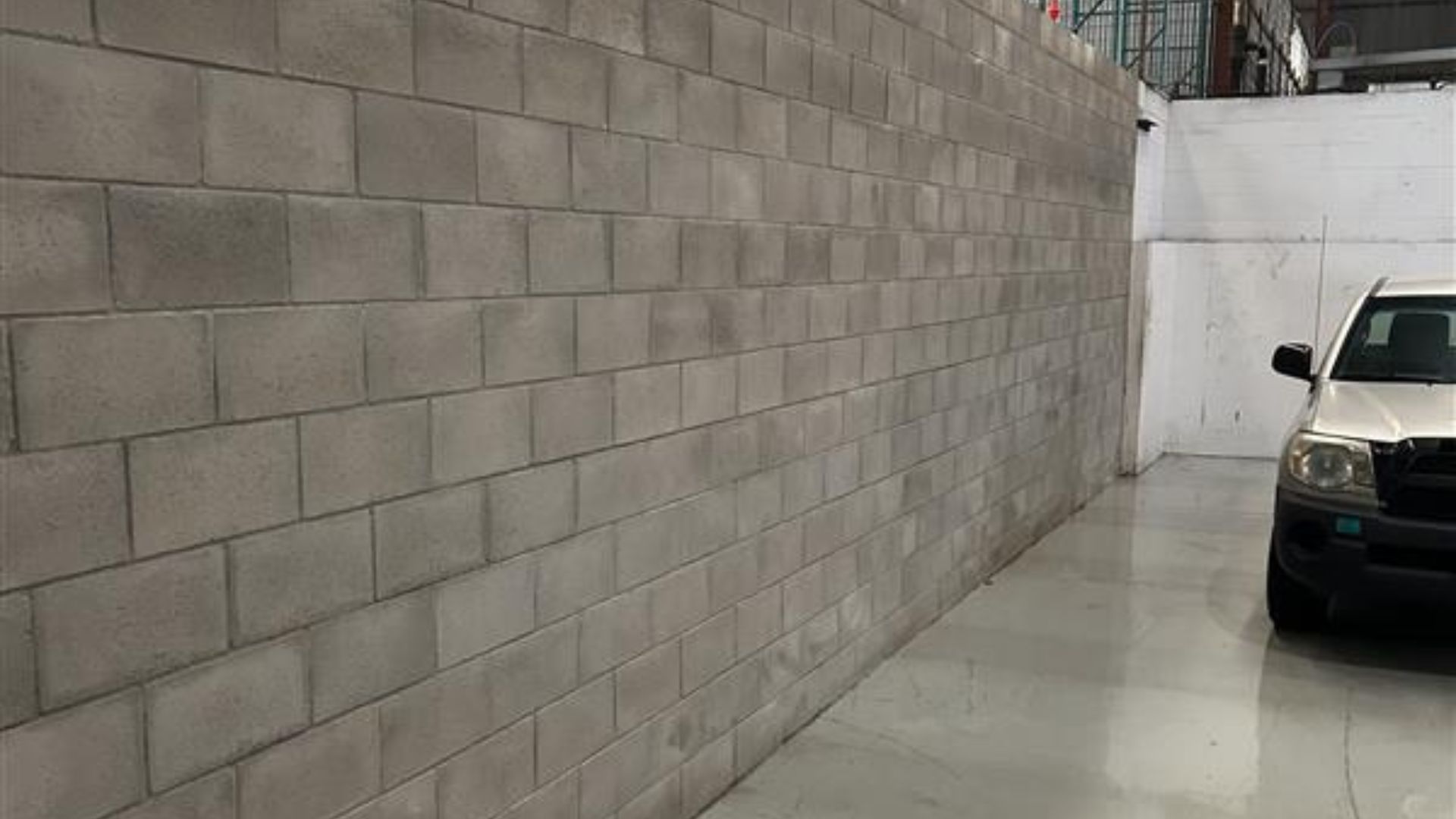 Long concrete wall beside a parked black SUV in a narrow indoor parking area