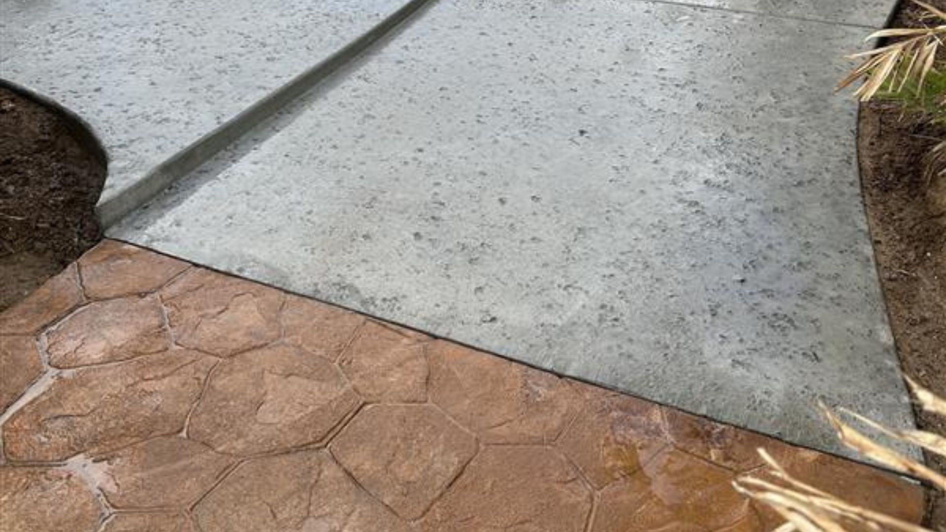 Concrete walkway meeting a reddish stamped patio beside mulch-lined garden edges