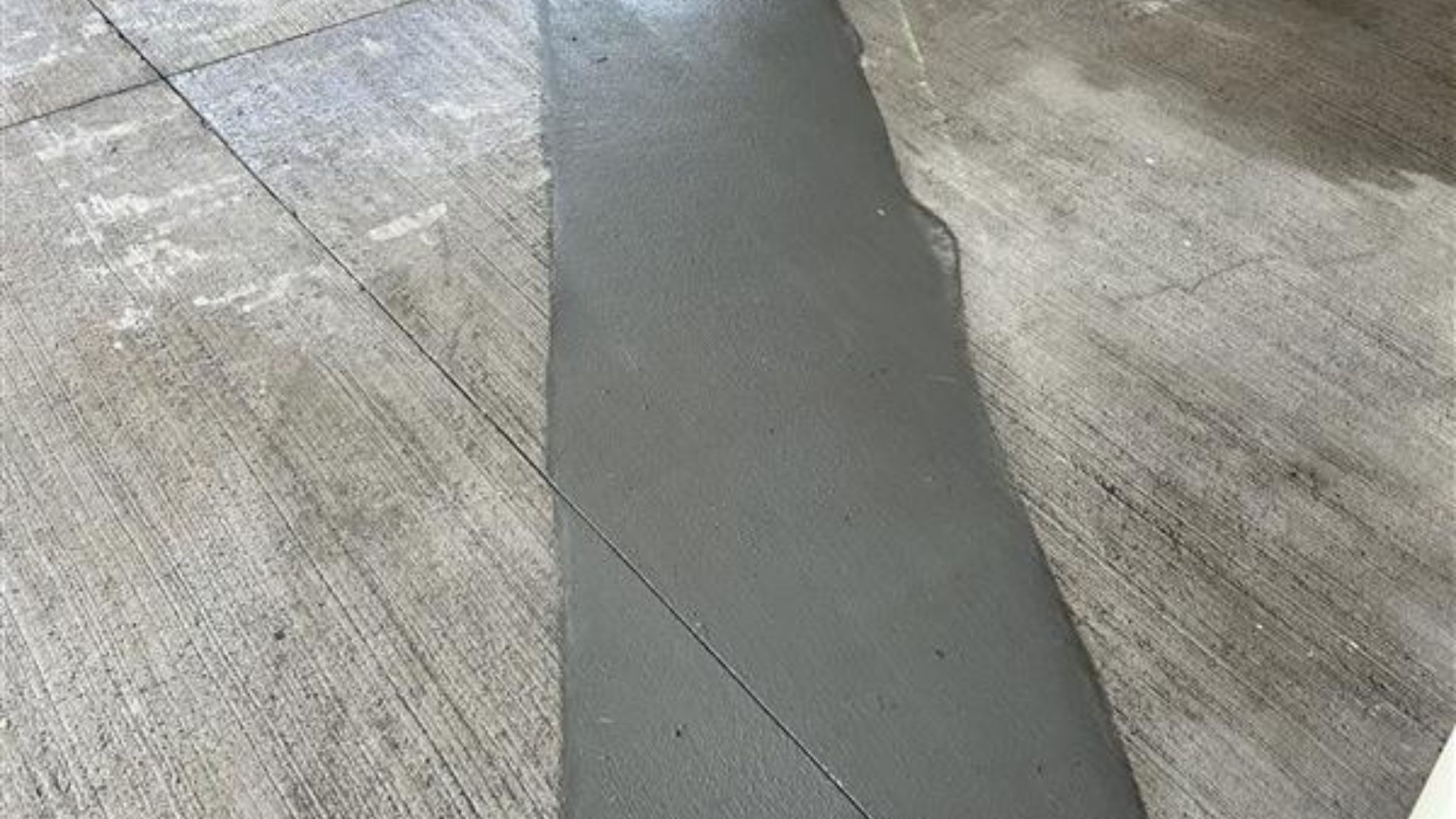Close-up of a concrete surface with a dark gray repaired crack running down the center.