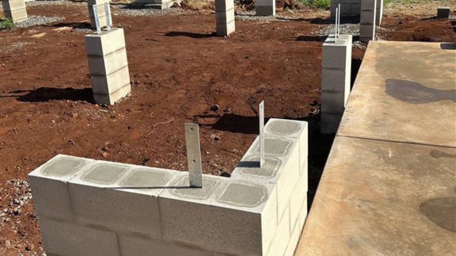 Partially built cinder block wall at a construction site on red dirt next to a concrete slab