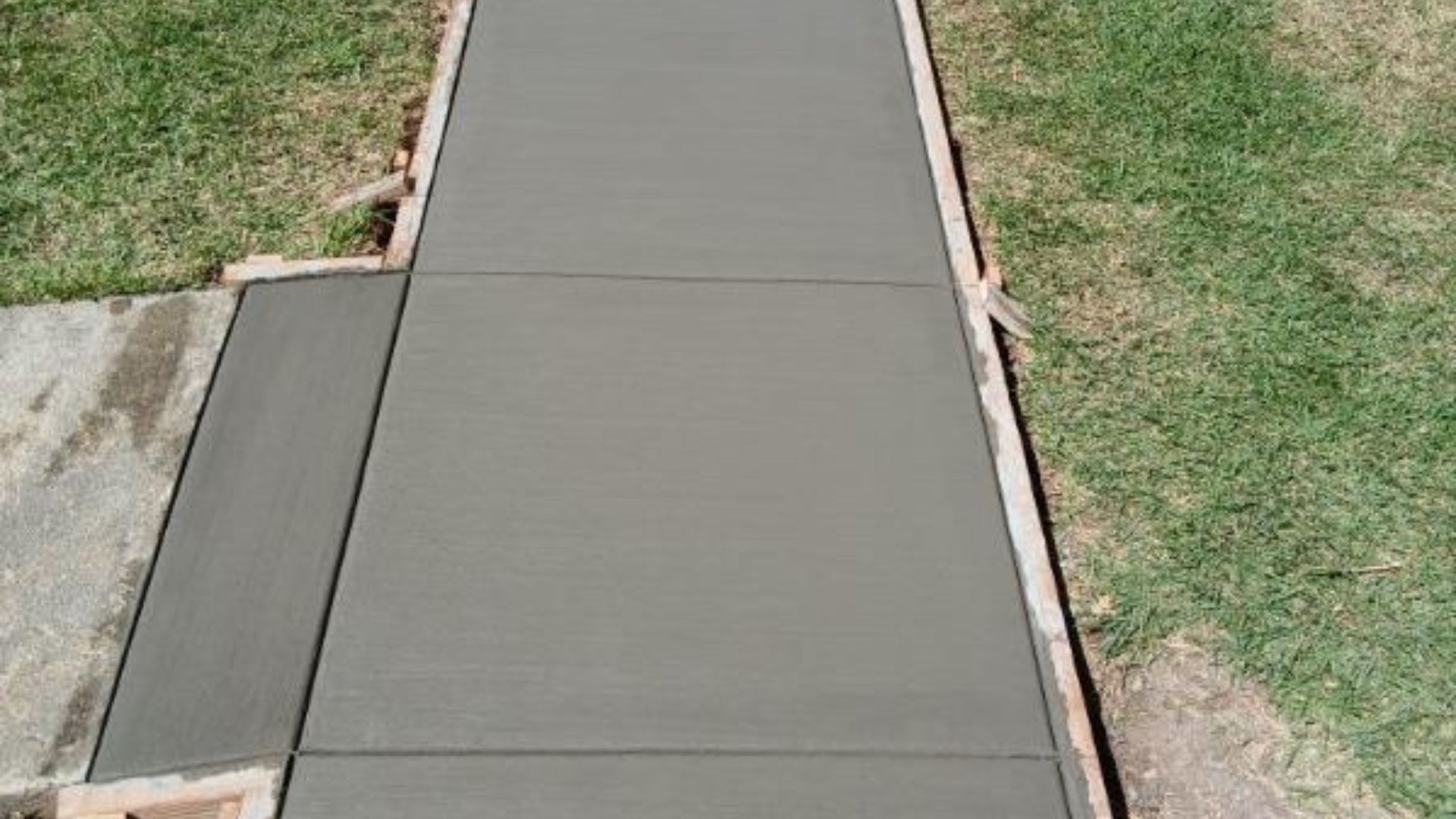 Concrete sidewalk ramp between grass lawns and a driveway edge