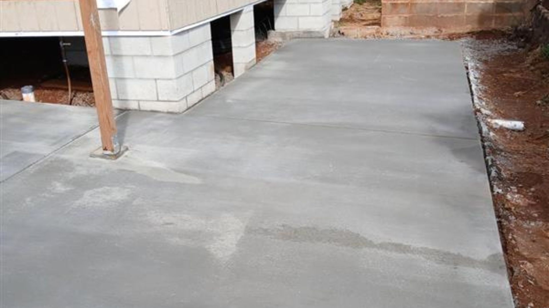 Concrete patio beside a house with a support post and unfinished dirt edge
