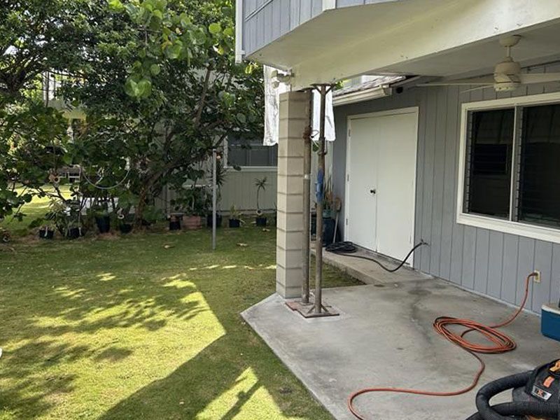 Backyard patio, a white house, and an orange hose on the concrete.