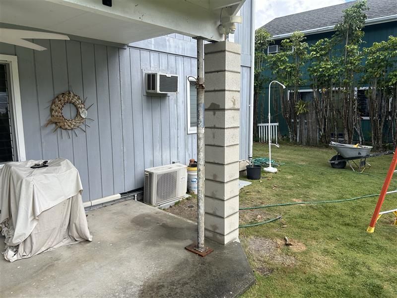 Covered patio with white siding, outdoor AC unit, and a grassy yard with a wheelbarrow and swing set.