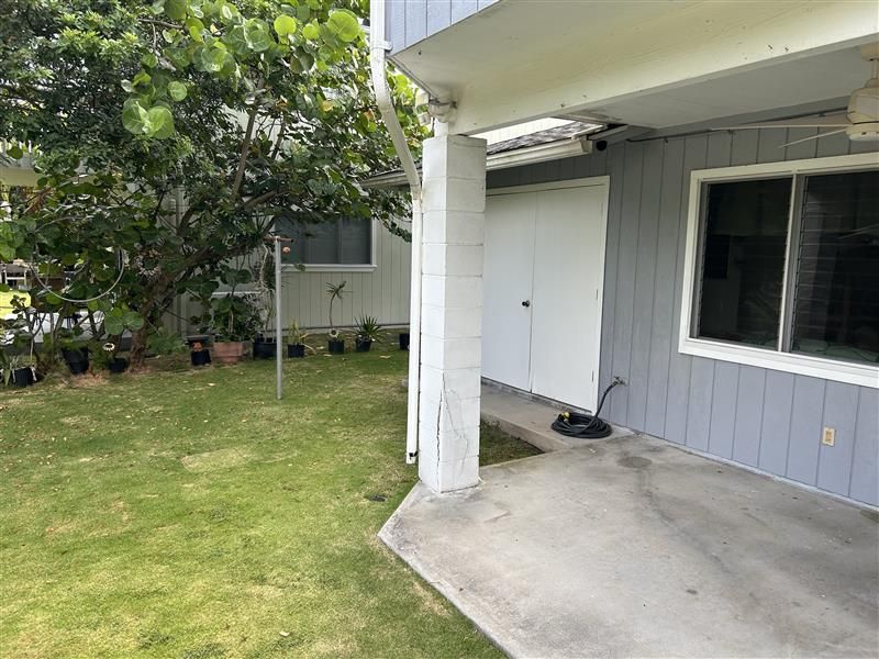 Backyard patio beside a gray house with a white column, sliding door, and green lawn tree