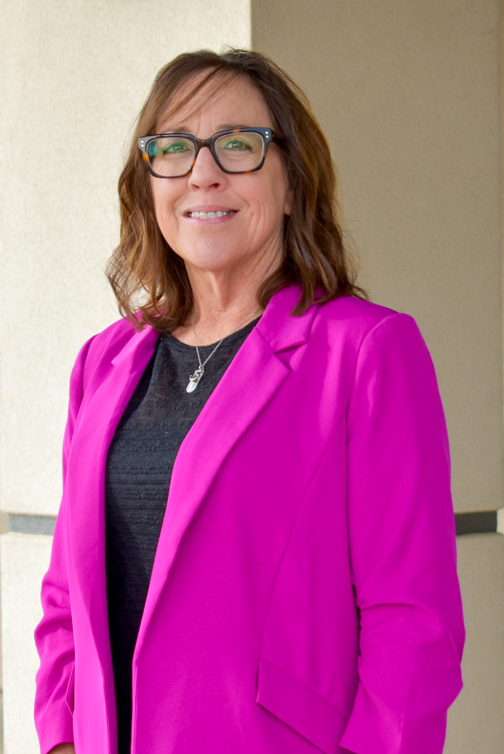 A woman wearing glasses and a sweater is smiling for the camera.